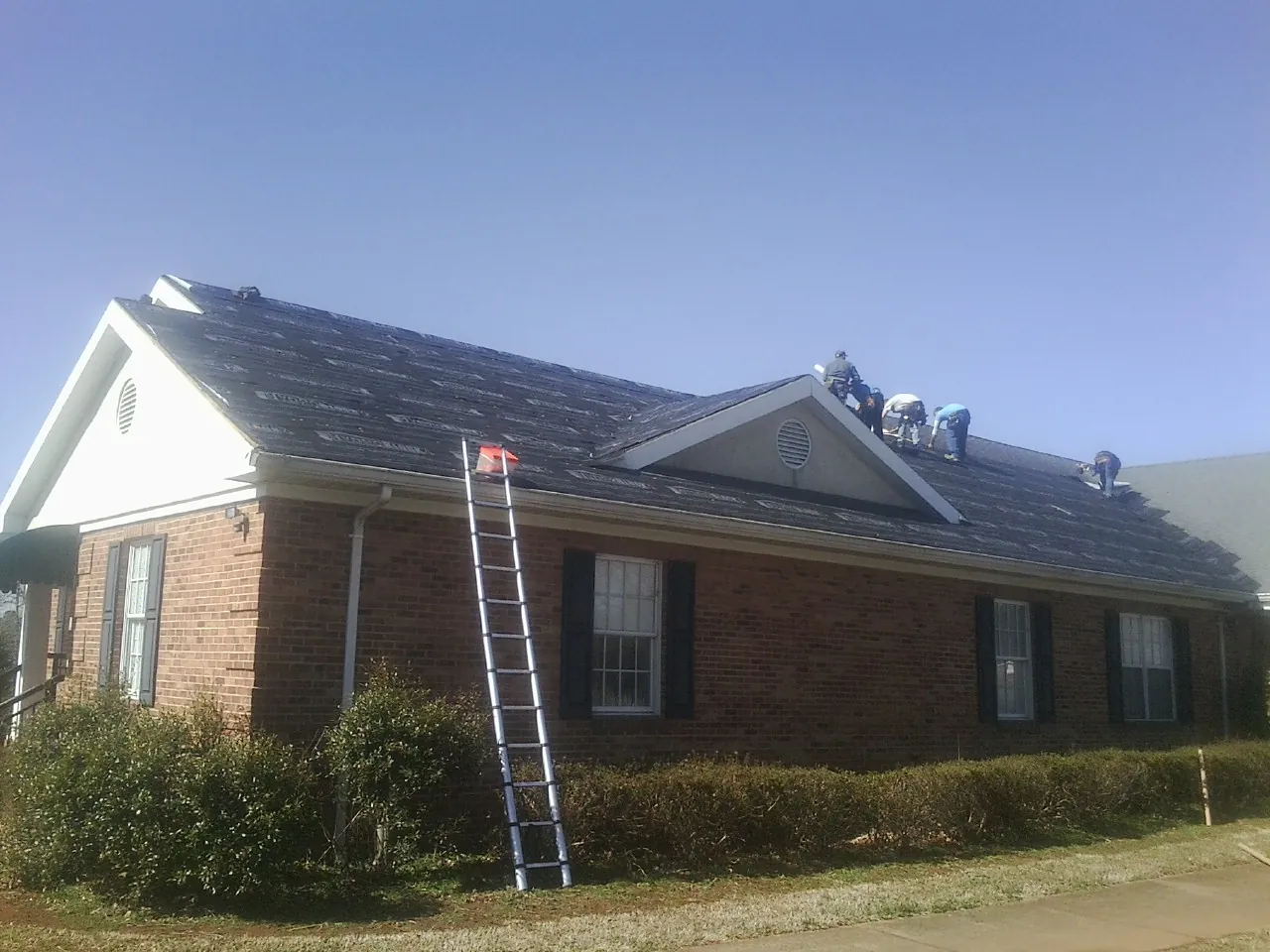 Crew tearing shingles off a brick ranch roof with a ladder set — Emergency Roof Repair work by our crew in Torrey