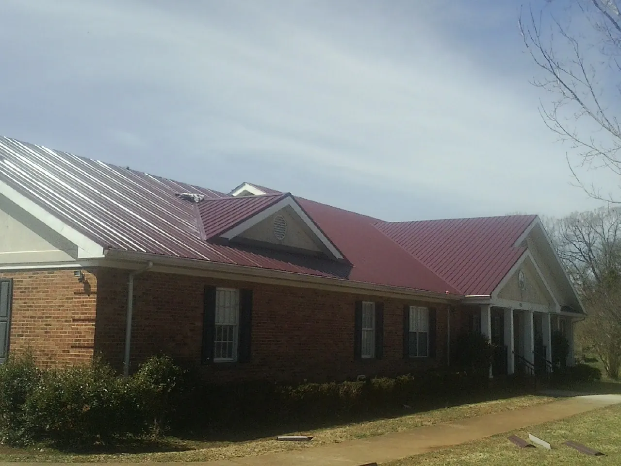 Red metal roof with gabled entries on a long brick building, from a Hail Damage Roof Repair job in Torrey