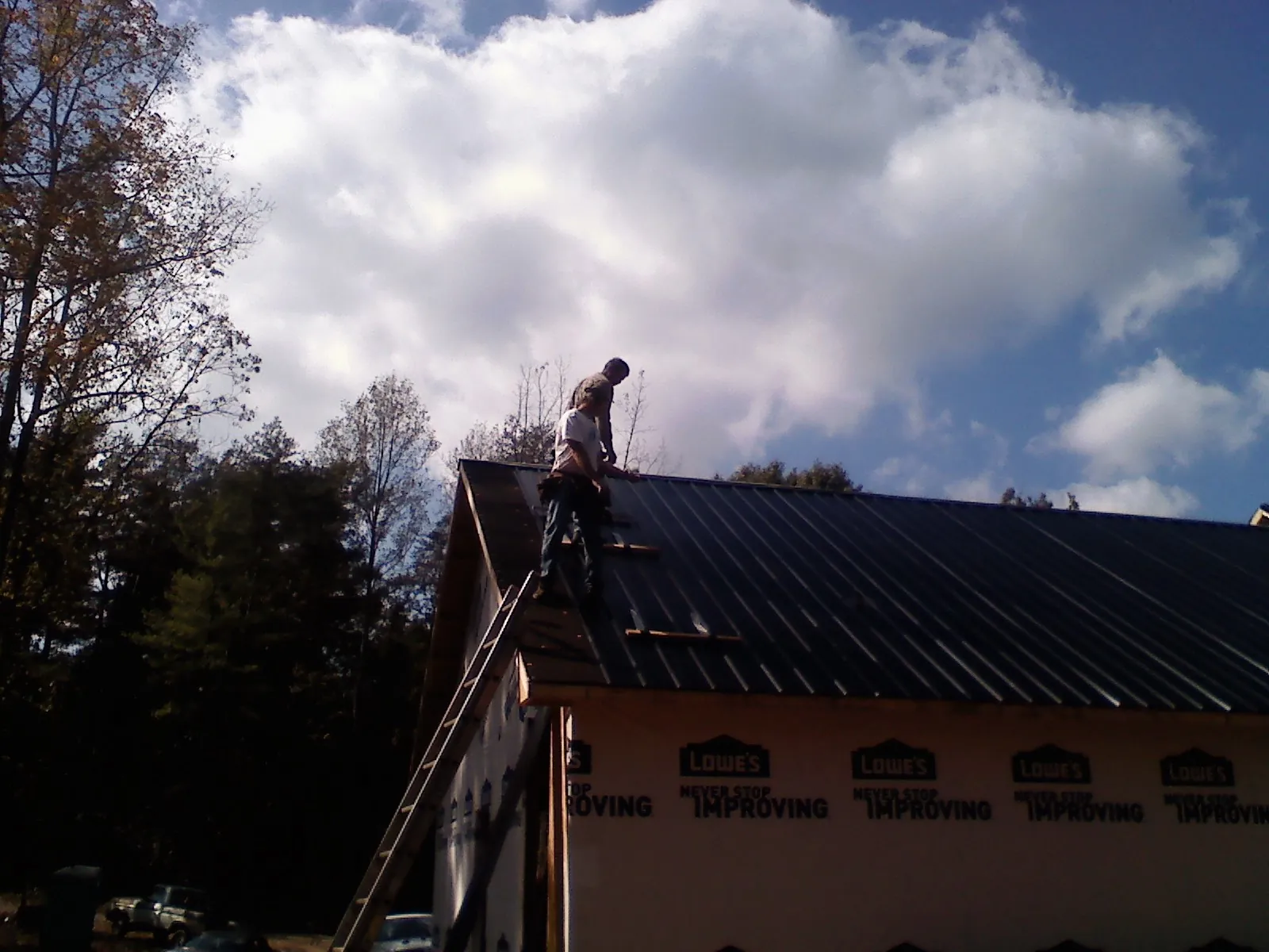 Roofer fastening dark metal panels high against a cloudy sky, from a Roof Inspection job in Torrey